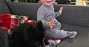 Jayce joined the competition — help win amazing prizes! toddler, child, dog, sofa, blanket, pajamas, smiling, indoor, home, living_room, furniture, pet, black_dog, gaming_chair, shelf, person, stairs, cozy, casual, relaxed