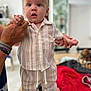baby, child, person, hands, pajamas, striped_clothing, indoor, table, foot, face, expression, standing, blurred_background, home, furniture, adult, holding, comfort, cozy, cute