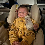 Khelid a rejoint le concours — aidez-le/la à gagner de superbes lots ! baby, infant, car_seat, bottle, milk, yellow_onesie, tiger_print, smile, feet, hands, face, cheeks, seat_padding, warning_label, clothing, indoor, soft_lighting, portrait, cute, cozy