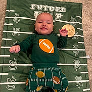 Colton is registered to the contest to win money with this photo: baby, child, smiling, football, blanket, clothing, green, orange, white, carpet, happy, cute, infant, socks, patterned_pants, lying_down, indoors, portrait, young_child, playful