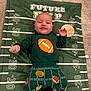 baby, child, smiling, football, blanket, clothing, green, orange, white, carpet, happy, cute, infant, socks, patterned_pants, lying_down, indoors, portrait, young_child, playful