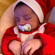 Noé participe au concours pour gagner de l'argent avec cette photo : baby, sleeping, pacifier, red_clothing, santa_hat, infant, hands, closeup, cute, cozy, blanket, soft_fabric, child, peaceful, indoors, portrait, newborn, holiday_theme, resting, warm_colors