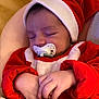 baby, sleeping, pacifier, red_clothing, santa_hat, infant, hands, closeup, cute, cozy, blanket, soft_fabric, child, peaceful, indoors, portrait, newborn, holiday_theme, resting, warm_colors