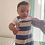 toddler, child, baby, striped_clothing, overalls, mattress, hand, indoor, curtain, pattern, support, standing, person, foot, bed, window, light, clothing, room, furniture