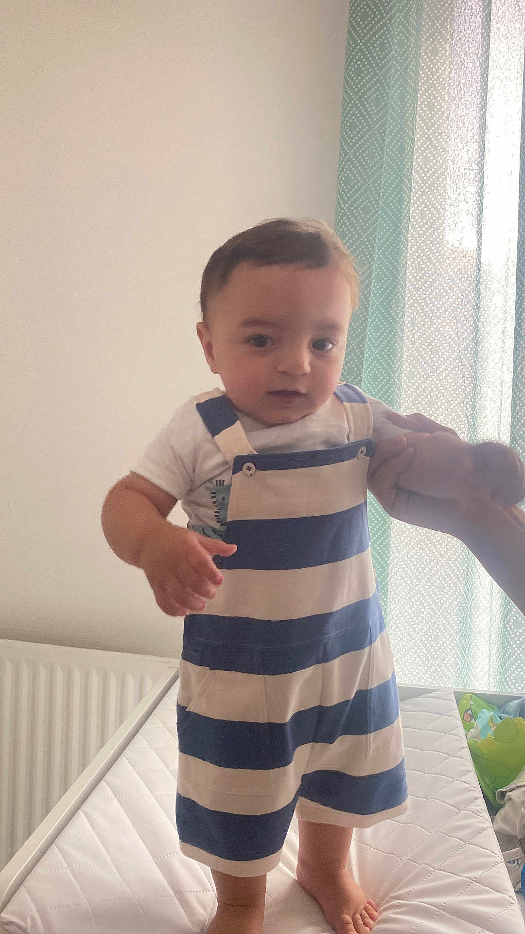 Amir participe au concours pour gagner de l'argent avec cette photo : toddler, child, baby, striped_clothing, overalls, mattress, hand, indoor, curtain, pattern, support, standing, person, foot, bed, window, light, clothing, room, furniture