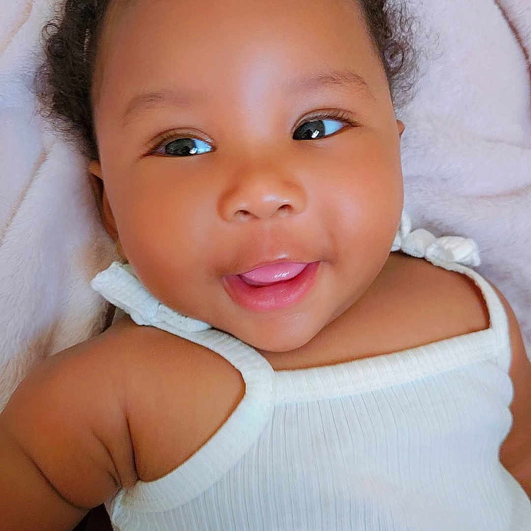 Amelia joined the competition — help win amazing prizes! adorable, baby, blanket, child, closeup, curly_hair, cute, expression, face, happy, head, infant, lying_down, person, pink_bow, portrait, skin, smiling, white_clothing, young