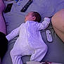 baby, sleeping, bed, onesie, remote_control, pacifier, pillow, phone, blanket, person, indoor, resting, infant, sleep, home, comfort, purple_light, furniture, relaxation, cozy