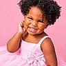 child, toddler, portrait, smiling, happy, curly_hair, pink_dress, formalwear, bow, tutu, sitting, studio, pink_background, fashion, cute, african_american, face, teeth, joyful, photography