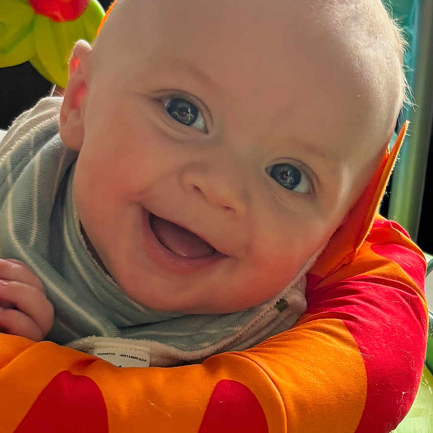 Hayes joined the competition — help win amazing prizes! baby, cheerful, child, closeup, colorful, cute, face, green, happy, indoor, infant, orange, pacifier, padded_ring, person, play_area, red, smiling, toy, young