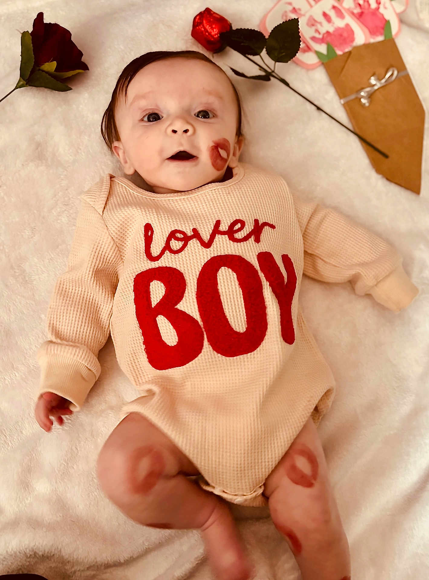 Ryden is registered to the contest to win money with this photo: baby, infant, child, onesie, red_text, kiss_mark, lipstick_mark, rose, bouquet, soft_blanket, portrait, cute, open_mouth, lying_down, indoor, cozy, gift_wrap, valentine_theme, legs, hands