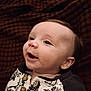 baby, infant, child, face, eyes, smile, blanket, clothing, button, pattern, portrait, close_up, cozy, soft_lighting, hair, ear, skin, mouth, lying_down, background_texture