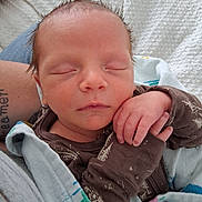 Everett is registered to the contest to win money with this photo: newborn, baby, sleeping, infant, portrait, face, closed_eyes, peaceful, cozy, blanket, swaddled, hand, brown_clothing, baby_hair, indoors, close_up, resting, parent, cuddling, photography