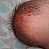 baby, newborn, infant, head, hair, fuzzy_hair, scalp, close_up, portrait, lying_down, bedding, blanket, patterned_background, indoors, cozy, skin, brown_hair, child, photograph, cropped