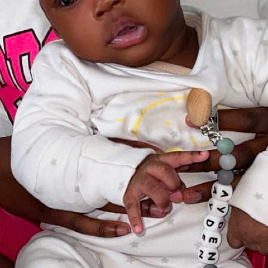 Ayden participe au concours pour gagner de l'argent avec cette photo : adult_hand, baby, child, closeup, curious, cute, face, hand, holding, indoor, infant, name_beads, onesie, pacifier_clip, person, seated, skin, soft_blanket, star_pattern, white_clothing