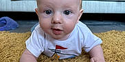 Theo joined the competition — help win amazing prizes! baby, infant, toddler, child, curious, lying_down, yellow_rug, white_shirt, mohawk, living_room, couch, blanket, floor, hands, face, eyes, expression, indoors, carpet, person