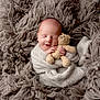 newborn, baby, sleeping, blanket, crocheted_toy, teddy_bear, soft_texture, cozy, wrapped, infant, cute, peaceful, portrait, child, hand, face, knitwear, warm, fuzzy, resting