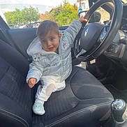 Maël a rejoint le concours — aidez-le/la à gagner de superbes lots ! child, toddler, car_interior, steering_wheel, seat, jacket, white_clothing, smiling, happy, seatbelt, dashboard, car_door, window, sky, trees, daylight, person, vehicle, cute, playful