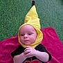 Eren joined the competition — help win amazing prizes! baby, infant, yellow_hat, black_shirt, red_pattern, pink_blanket, green_background, child, cute, lying_down, hands, headwear, expression, indoors, portrait, clothing, baby_face, young_child, soft_texture, playful_costume