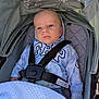 baby, child, stroller, hoodie, blanket, seatbelt, blue_eyes, face, infant, clothing, baby_clothes, outdoor, sunlight, canopy, soft_texture, comfort, sitting, portrait, casual, young_child