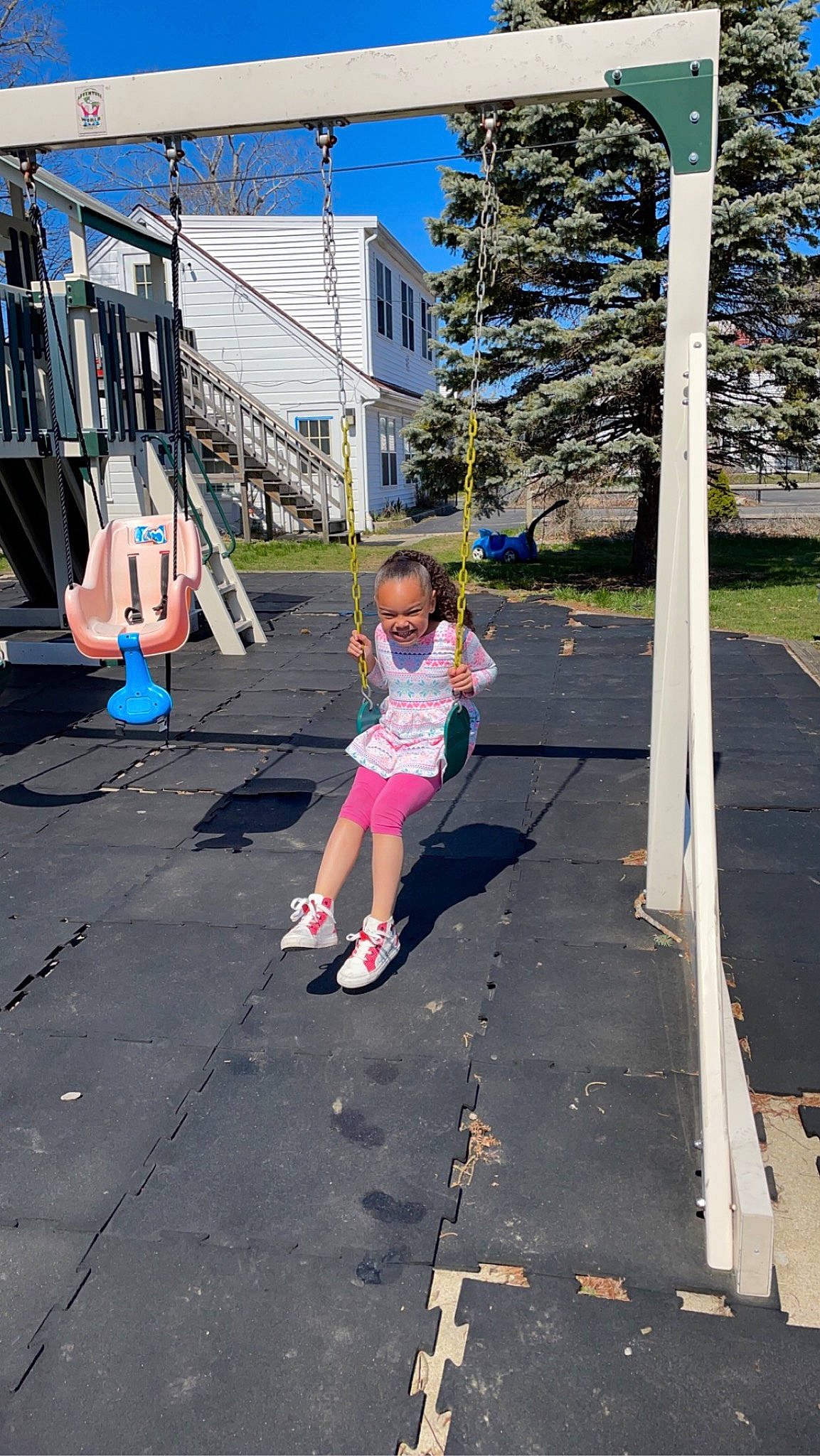 Jaelisse is registered to the contest to win money with this photo: asphalt, child, city, electric_blue, fun, house, joy, leisure, outdoor_play_equipment, pedestrian, person, plant, playground, recreation, road, road_surface, sidewalk, sky, street, swing