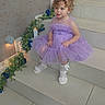 bow, child, curly_hair, cute, decor, dress, flowers, girl, greenery, indoor, lavender, portrait, shoes, sitting, smiling, socks, stairs, tiles, toddler, young_child