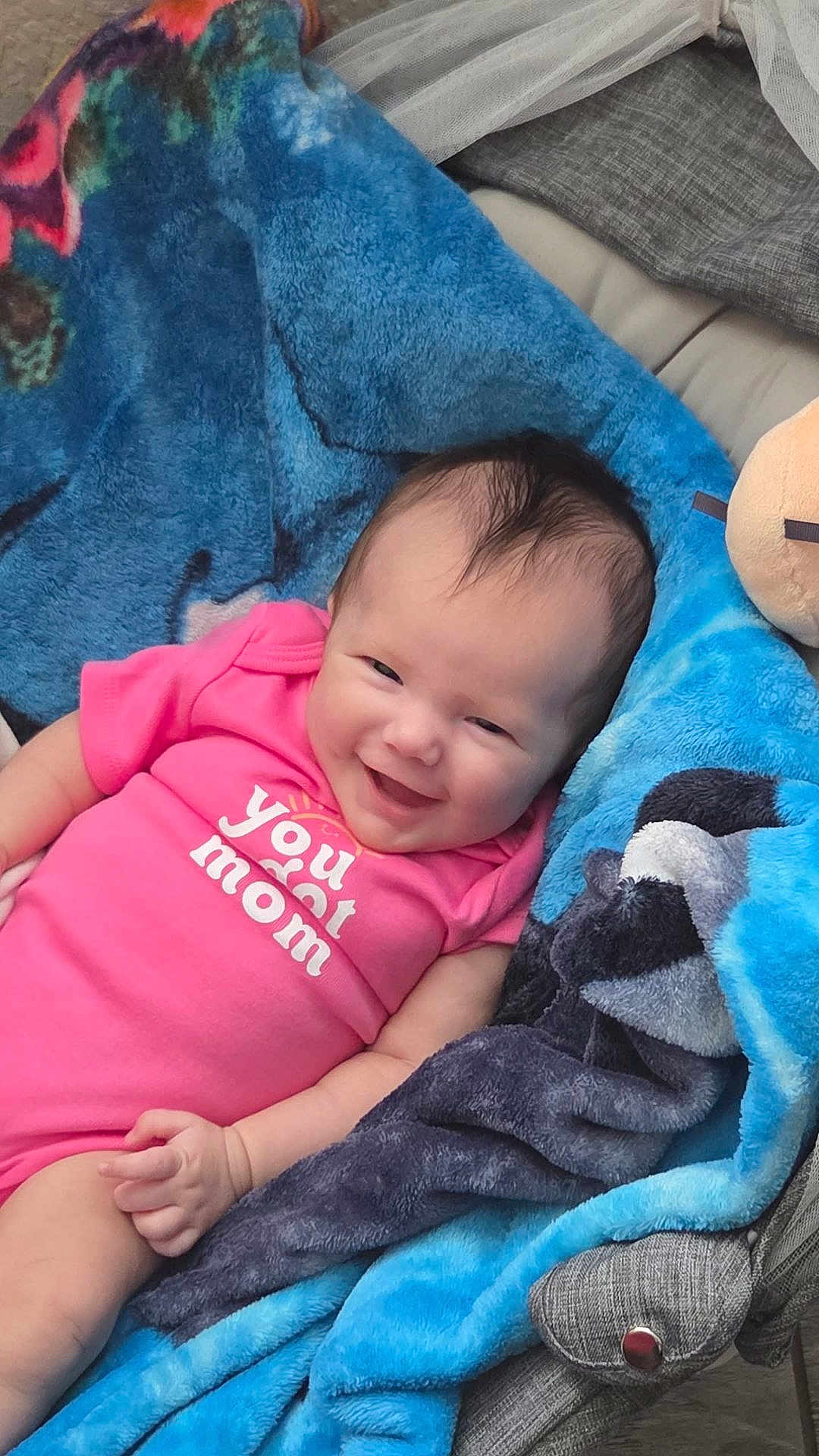 Marlee is registered to the contest to win money with this photo: baby, infant, smiling, pink_onesie, blanket, blue_blanket, gray_blanket, happy, cute, child, portrait, sitting, cozy, indoor, person, skin, head, hand, clothing, fabric