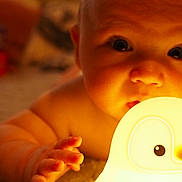 Hugo is registered to the contest to win money with this photo: baby, child, infant, hand, face, light, night_light, toy, penguin, carpet, indoor, closeup, cute, warm_light, skin, expression, curious, soft_texture, portrait, baby_toy