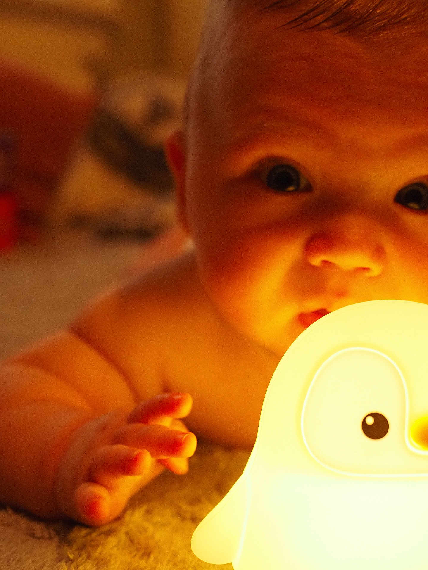 Hugo is registered to the contest to win money with this photo: baby, child, infant, hand, face, light, night_light, toy, penguin, carpet, indoor, closeup, cute, warm_light, skin, expression, curious, soft_texture, portrait, baby_toy