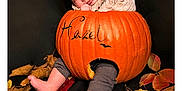 Hazel is registered to the contest to win money with this photo: baby, pumpkin, autumn_leaves, fall, cute, infant, orange, black_background, seasonal, child, portrait, legs, feet, cozy, cute_expression, decor, holiday, nature, sitting, costume