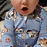 baby, child, onesie, blue_clothing, cartoon_print, cute, indoor, person, infant, surprised_expression, hands, feet, sitting, face, wide_eyes, open_mouth, pajamas, young_child, bed, cozy