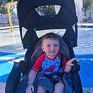Jaxson is registered to the contest to win money with this photo: toddler, stroller, child, blue_eyes, towel, pool, water_splash, outdoor, sunny, swim_shirt, spiderman, seatbelt, playground, summer, happy, baby, person, recreation, daylight, smile
