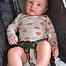 baby, child, stroller, onesie, pumpkin_pattern, blue_eyes, infant, cute, legs, hands, sitting, seatbelt, comfort, indoor, closeup, portrait, expression, soft_lighting, casual, relaxed