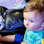 Jaxson is registered to the contest to win money with this photo: baby, blanket, blue_eyes, car_seat, casual_clothing, child, cozy, curly_hair, cute, home, indoor, infant, leather_couch, person, relaxed, sitting, sleeping, striped_clothing, toddler, young_child