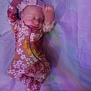 Emma is registered to the contest to win money with this photo: baby, sleeping, onesie, headband, floral_pattern, purple, blanket, infant, child, cute, peaceful, soft_lighting, motion_blur, lying_down, newborn, adorable, sleepwear, indoor, portrait, infancy