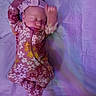 baby, sleeping, onesie, headband, floral_pattern, purple, blanket, infant, child, cute, peaceful, soft_lighting, motion_blur, lying_down, newborn, adorable, sleepwear, indoor, portrait, infancy