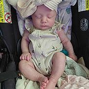 Emma is registered to the contest to win money with this photo: baby, blanket, bow, car_seat, child, clothing, cute, headband, indoor, infant, newborn, onesie, peaceful, person, resting, sleeping, small_feet, small_hands, soft_toys, toddler