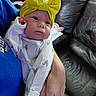 Emma is registered to the contest to win money with this photo: baby, infant, headband, yellow_bow, onesie, chicken_print, hand, adult, blue_shirt, leather_couch, indoor, person, child, cute, portrait, newborn, soft_lighting, cozy, holding, home
