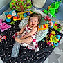 baby, child, playmat, toy, pillow, water_bottle, dress, smile, happy, indoor, plush_toy, colorful, cushion, floor_mat, infant, person, cute, play_area, soft_toy, cheerful