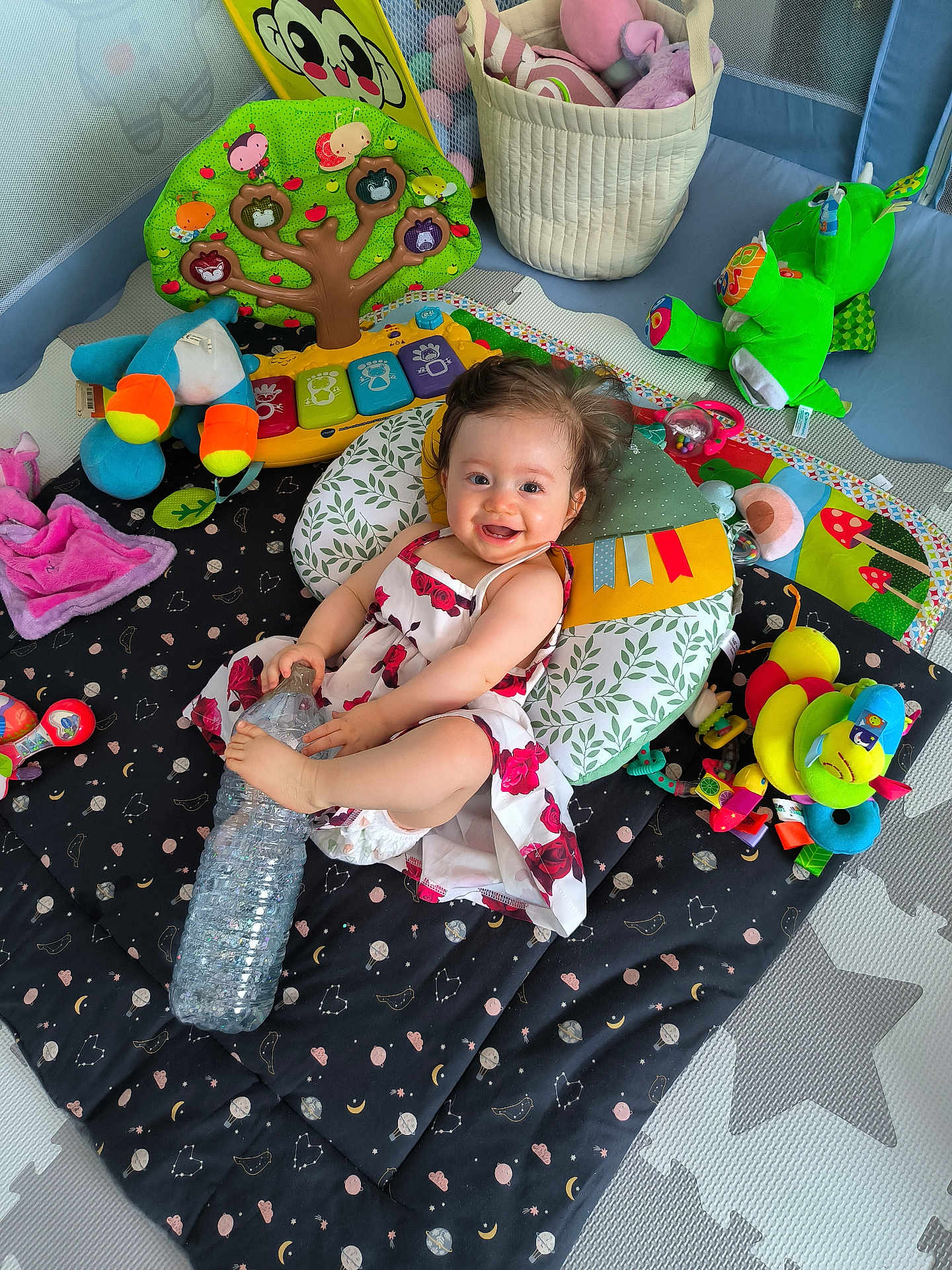 Kiara participe au concours pour gagner de l'argent avec cette photo : baby, child, playmat, toy, pillow, water_bottle, dress, smile, happy, indoor, plush_toy, colorful, cushion, floor_mat, infant, person, cute, play_area, soft_toy, cheerful