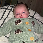 Layan participe au concours pour gagner de l'argent avec cette photo : baby, knitted_clothing, green_outfit, hedgehog_pattern, bedspread, indoor, portrait, infant, cute, toddler, buttoned_sweater, lying_down, face, person, home, warm_clothing, soft_texture, hair, expression, resting