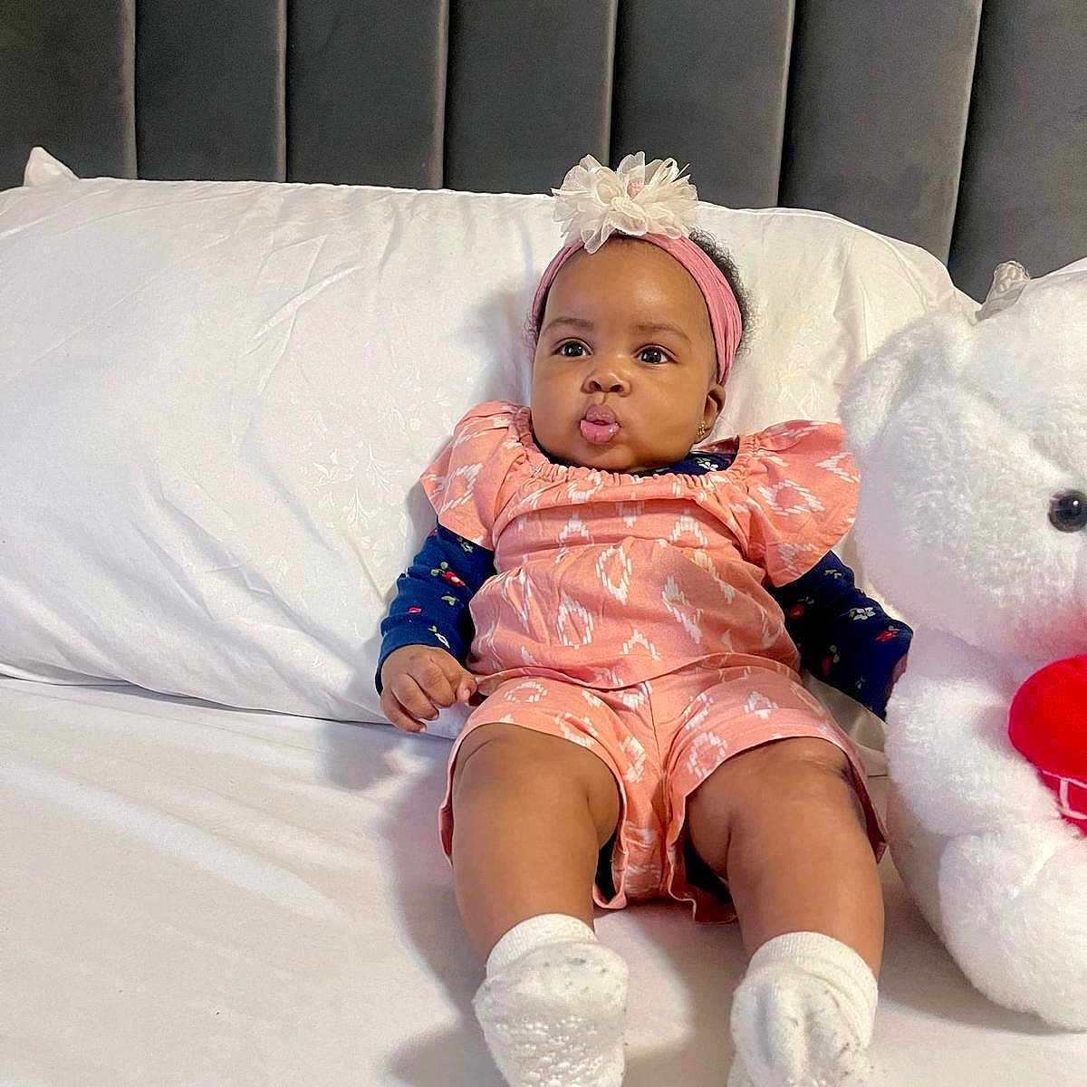 Oasi joined the competition — help win amazing prizes! adorable, baby, bed, child, cute, flower, furniture, headband, indoor, infant, pillow, pink_outfit, plush, portrait, pouty_face, sitting, soft_toy, stuffed_animal, teddy_bear, white_socks