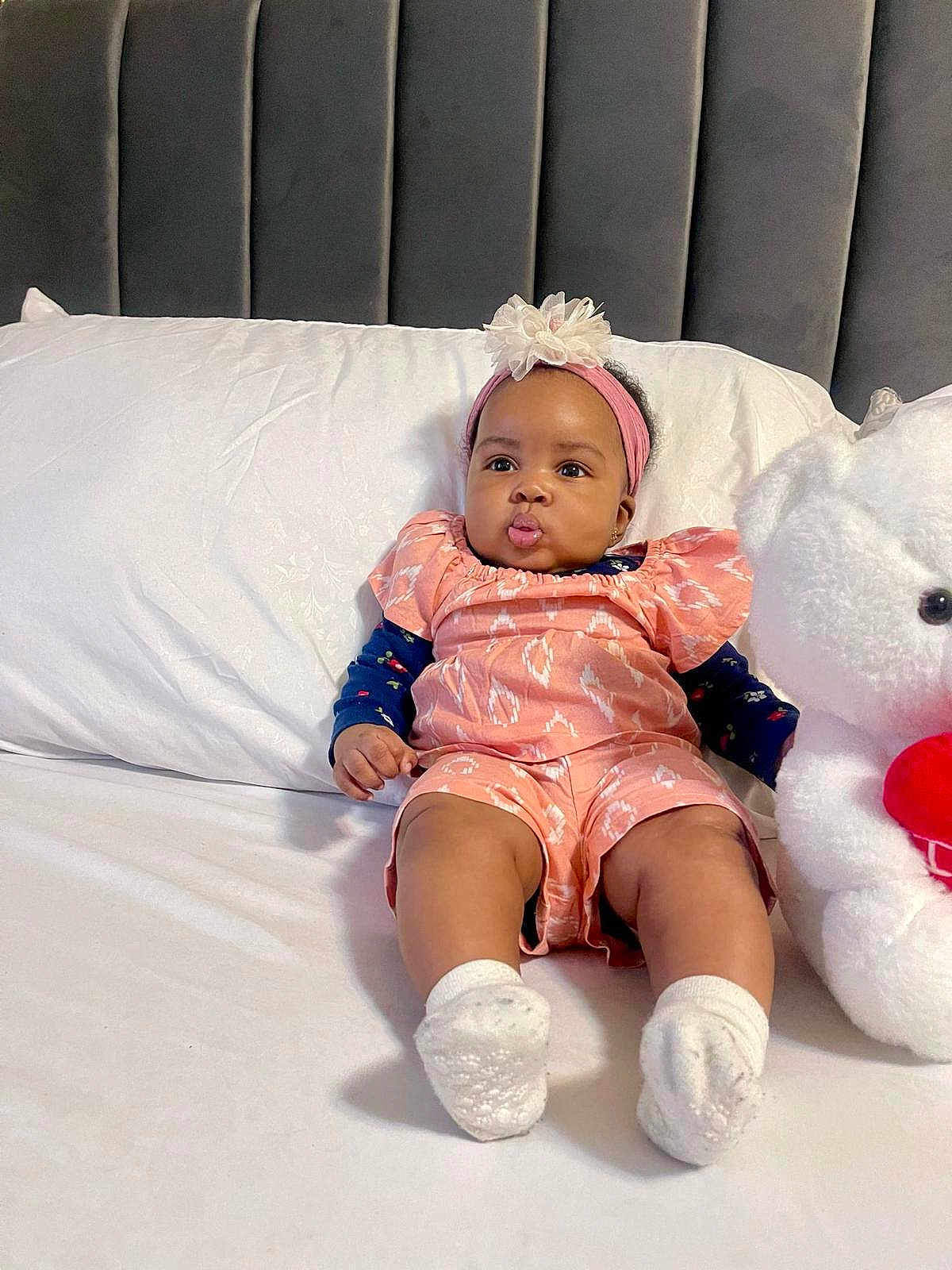 Oasi joined the competition — help win amazing prizes! adorable, baby, bed, child, cute, flower, furniture, headband, indoor, infant, pillow, pink_outfit, plush, portrait, pouty_face, sitting, soft_toy, stuffed_animal, teddy_bear, white_socks