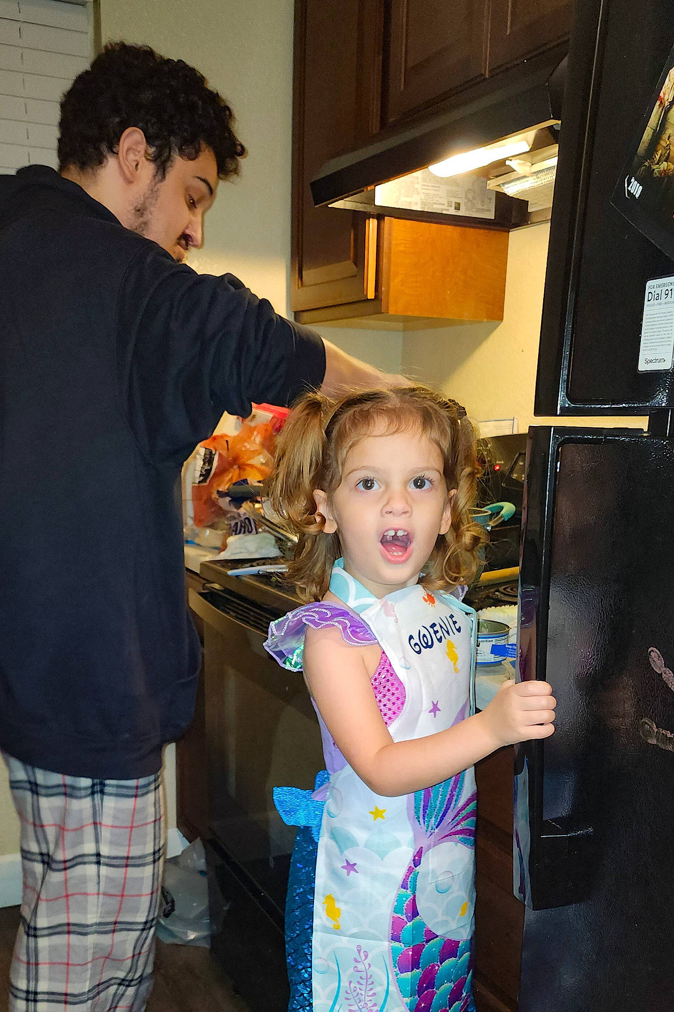 Gwendolyn is registered to the contest to win money with this photo: cabinetry, child, cooking, event, fashion_design, fun, gesture, happy, joint, kitchen, kitchen_appliance, pattern, person, plaid, refrigerator, room, shorts, standing, surprise, t_shirt