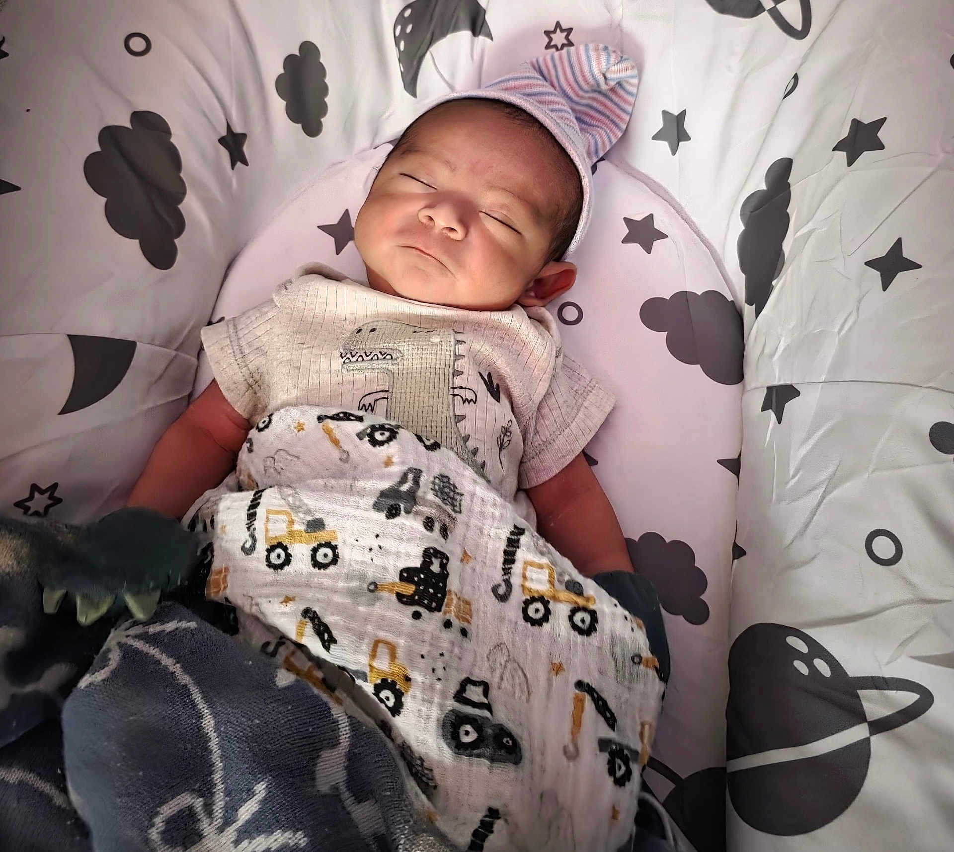 Thiago joined the competition — help win amazing prizes! baby, newborn, sleeping, blanket, hat, dinosaur, patterned_clothing, cushion, space_theme, stars, clouds, planet, infant, cozy, indoors, cute, child, resting, soft, portrait