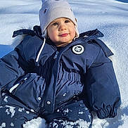 Jahyah a rejoint le concours — aidez-le/la à gagner de superbes lots ! baby, beanie, boots, child, cold_weather, hat, houses, outdoor, play, portrait, rosy_cheeks, sitting, smile, snow, snowsuit, snowy_landscape, sunlight, toddler, trees, winter_coat