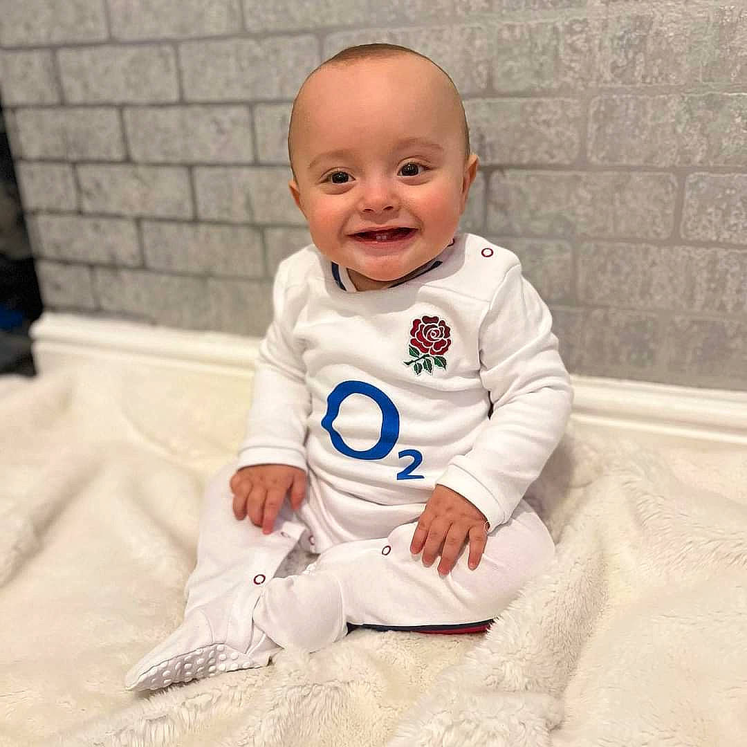 Harlan is registered to the contest to win money with this photo: baby, baby_products, baby_toddler_clothing, carmine, comfort, eye, face, flooring, gesture, hand, happy, head, joy, linens, long_sleeved_t_shirt, person, room, sleeve, smile, sportswear