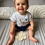 Livia a rejoint le concours — aidez-le/la à gagner de superbes lots ! baby, child, smiling, sitting, bed, pillow, white_shirt, flowers, navy_shorts, skin, foot, hand, hair_clip, indoor, cute, portrait, infant, happy, human, month_marker