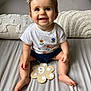 baby, child, smiling, sitting, bed, pillow, white_shirt, flowers, navy_shorts, skin, foot, hand, hair_clip, indoor, cute, portrait, infant, happy, human, month_marker