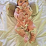 baby, infant, onesie, pink_clothing, cat_print, bed, pillow, plush, hand_in_mouth, cute, child, soft, sleepwear, head_support, lying_down, indoor, person, young_child, cozy, resting