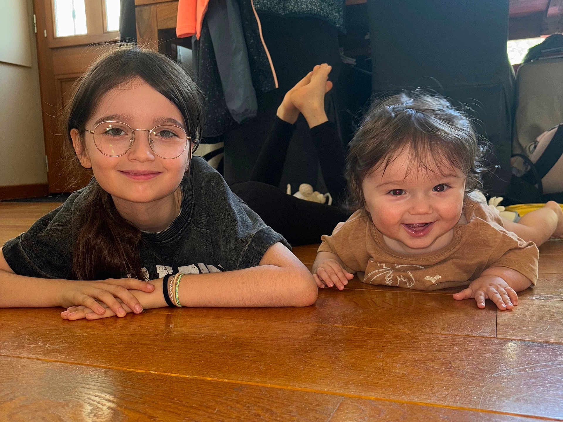Léo participe au concours pour gagner de l'argent avec cette photo : child, baby, glasses, smile, indoor, wooden_floor, sibling, happy, casual_clothing, long_hair, short_hair, portrait, person, floor, candid, home, natural_light, cute, family, relaxed